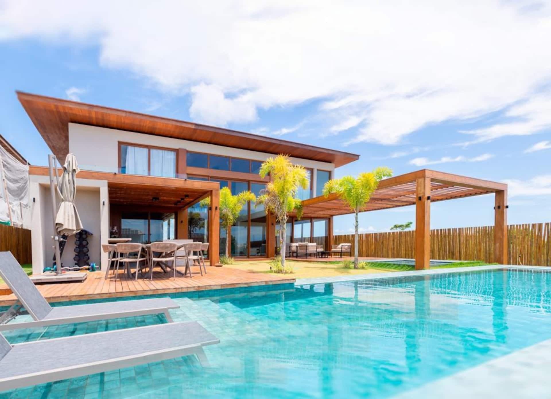 Casa Torres de dia, com piscina turquesa, deck de madeira e pergolado