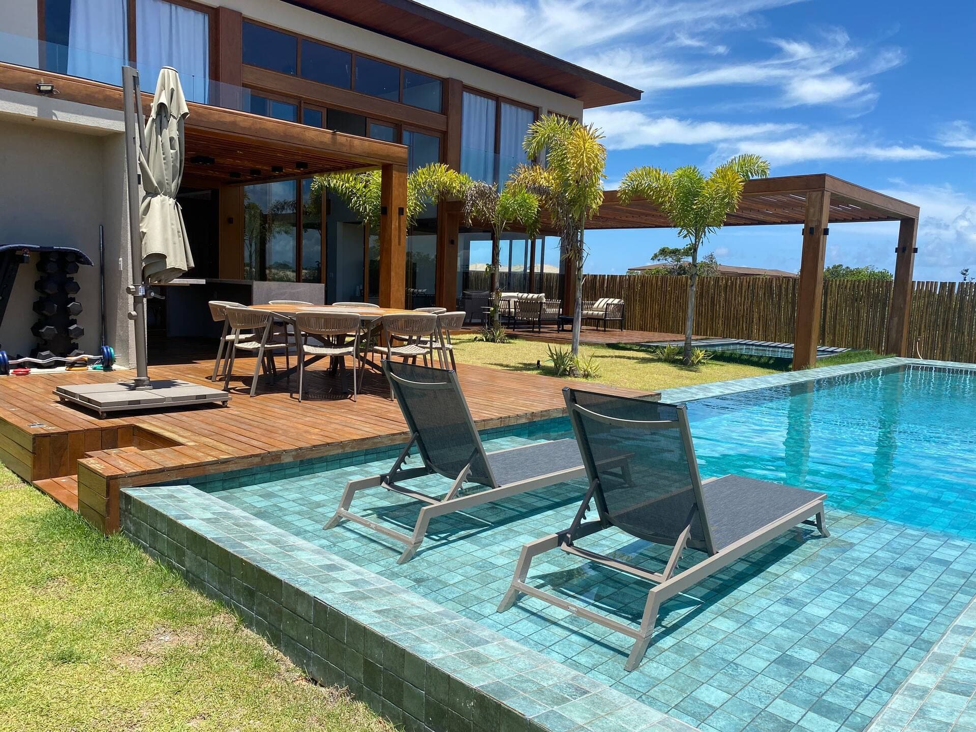 Espreguiçadeiras na própria piscina e mesa externa sobre o deck de madeira