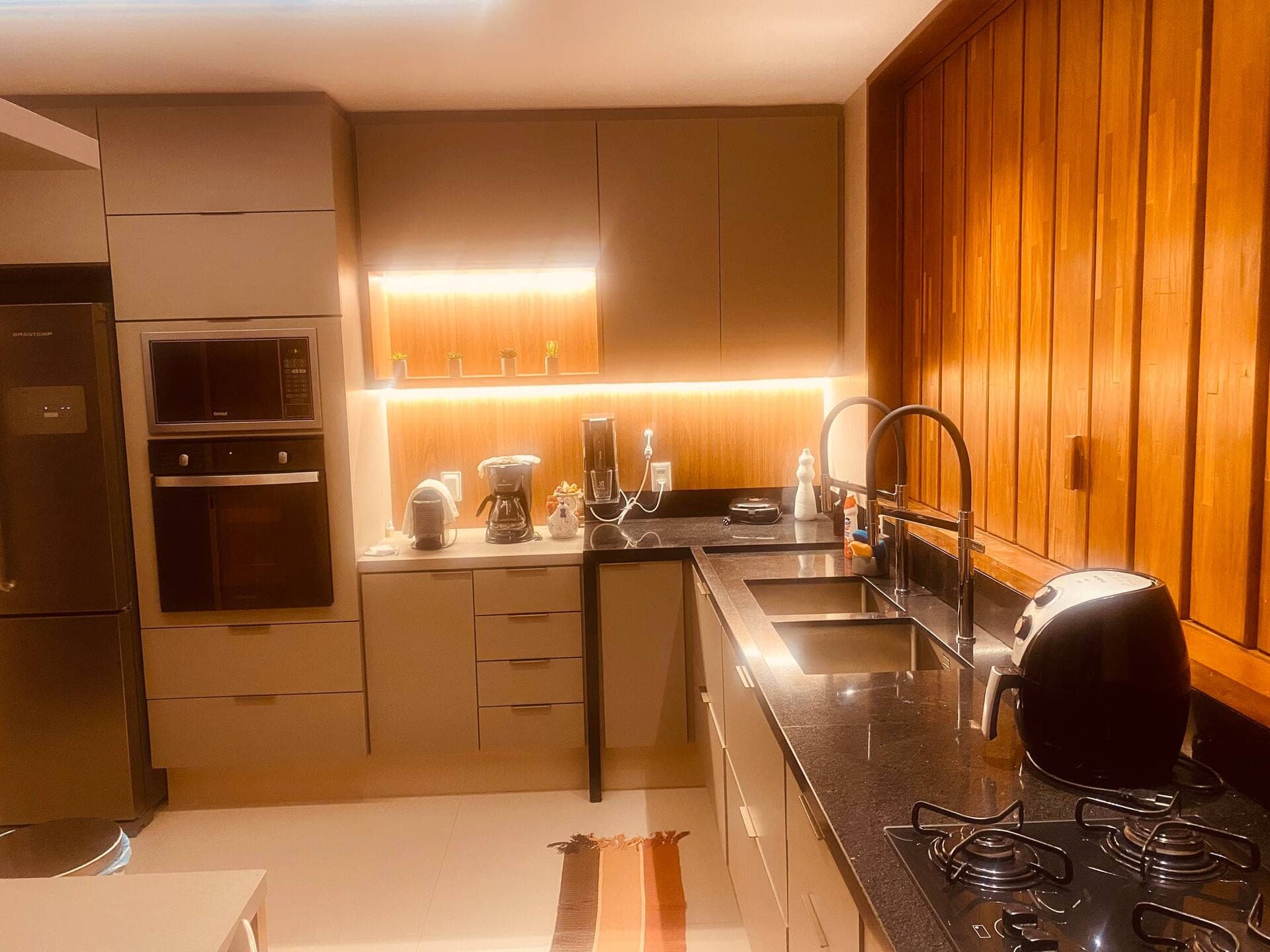 Cozinha com armários claros, painel de madeira e bancada escura