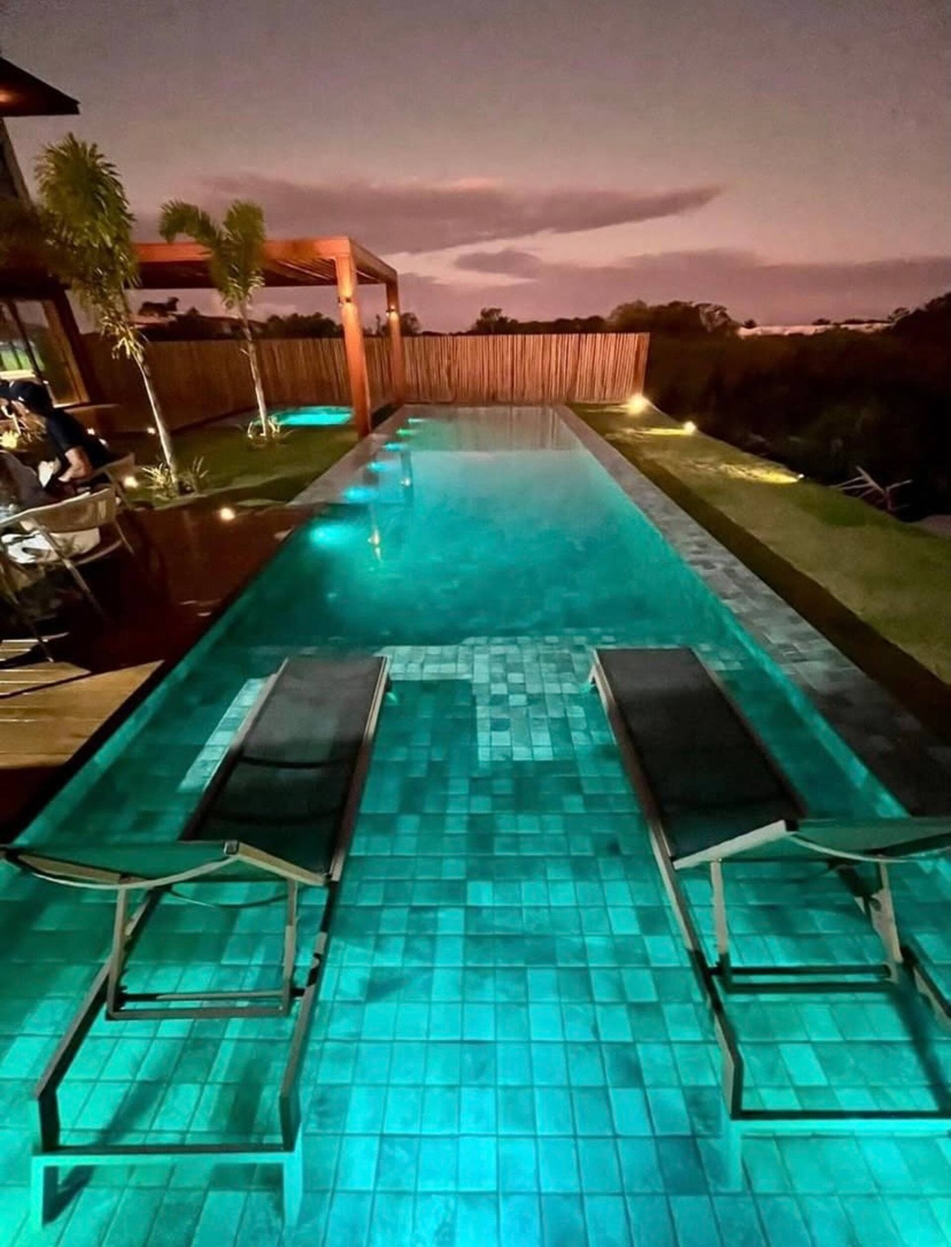 Piscina longa ao entardecer, com duas espreguiçadeiras