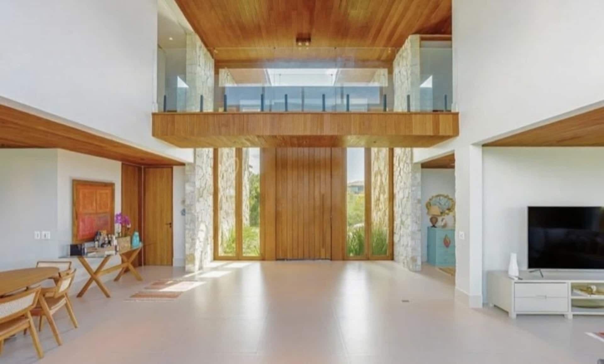 Hall de entrada com pé-direito duplo, mezanino de vidro e porta de madeira